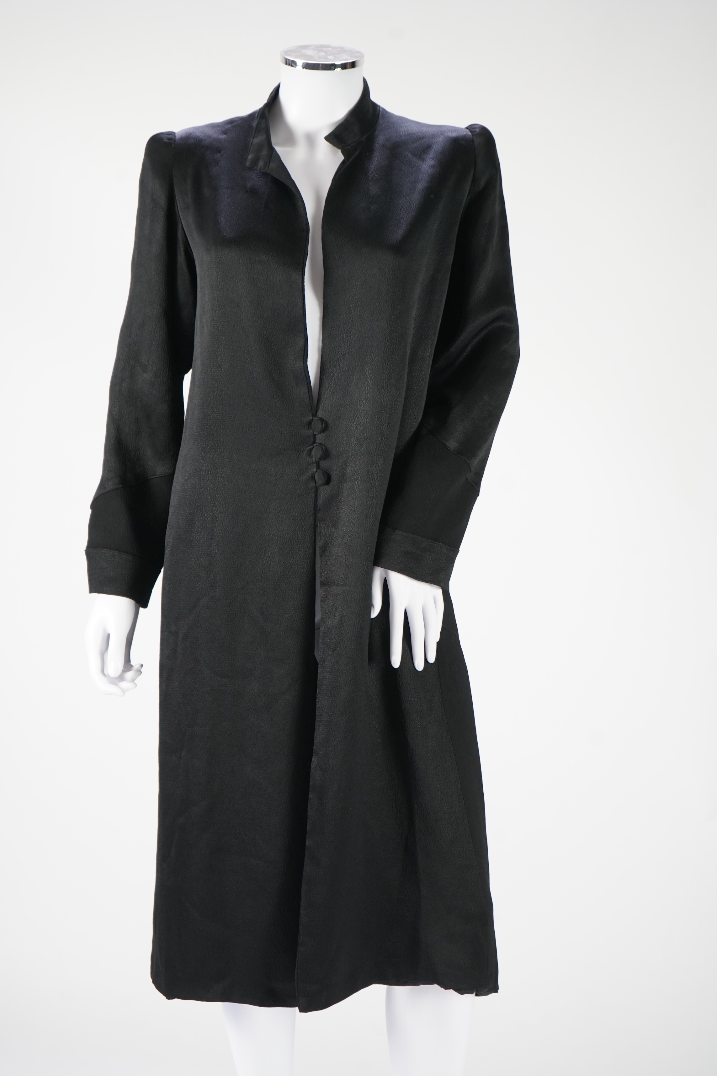 A 1930's black satin evening coat, with small collar and covered buttons to the front. Decorated with chevron motifs at side and lower sleeve detailing, front under arm width 19 inches, length back: top of collar to bott